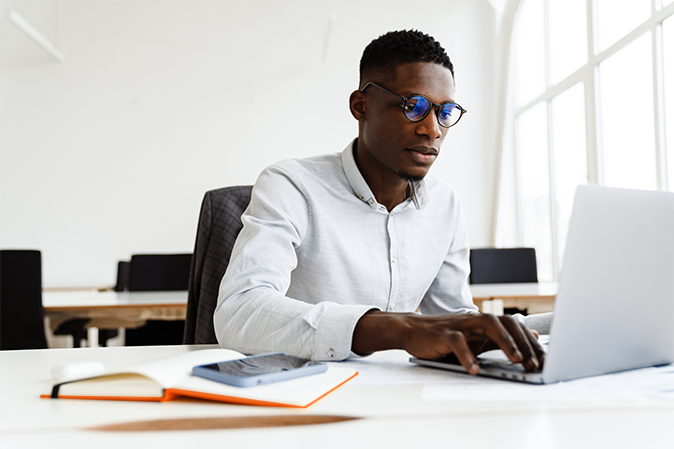 Afro american focused man in eyeglasses working with laptop while sitting in office