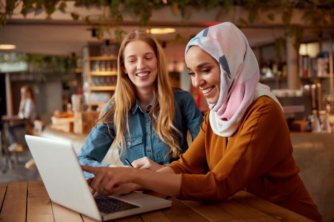 Two young woman working together on a laptop in a classroom