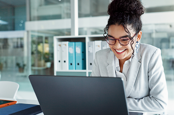 Young woman dressed professionally in an office smiling in front of a laptop