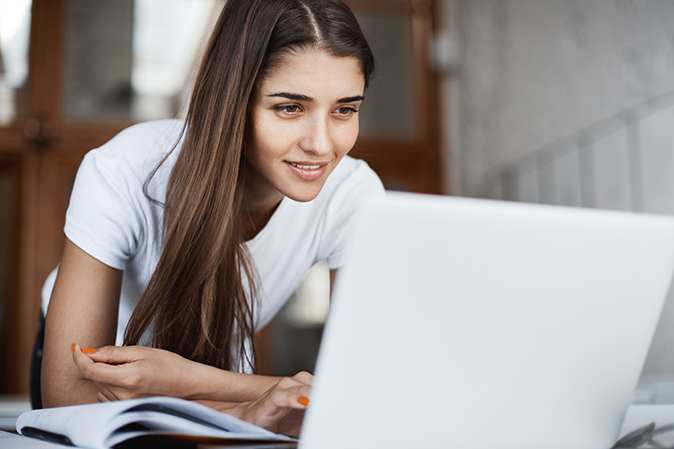 Young woman leaning forward onto a desk in front of a laptop with an open notebook