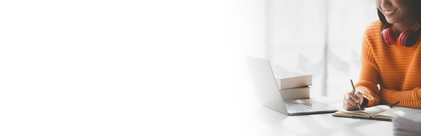 Young woman smiling as she's taking notes while watching something on her laptop