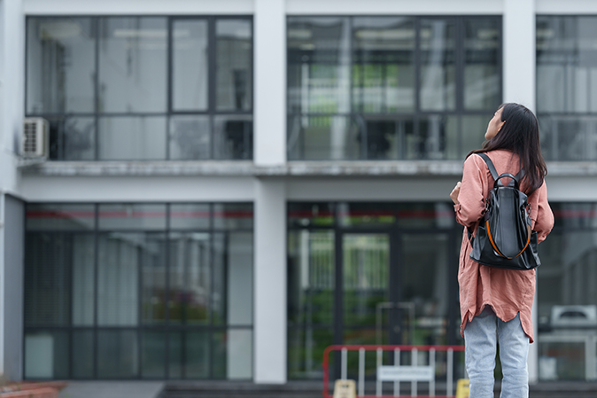 Young woman wearing a backpack looking at a school building