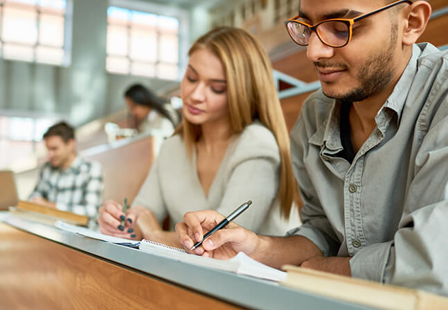Several college students writing notes in a lecture hall
