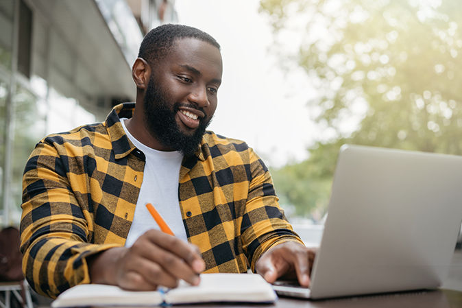 Young man writing notes while working on laptop