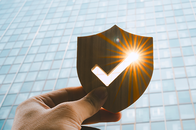 Hand holding a badge with a checkmark in front of a building outside