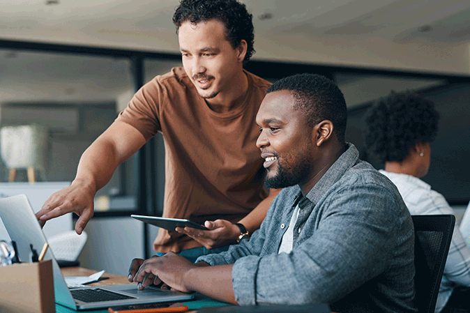 Two young men working together on a laptop in an office