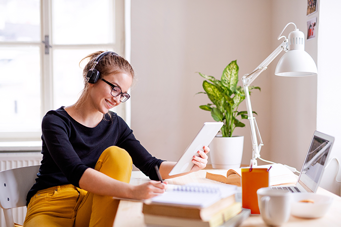 Young woman sitting at her desk at home studying with headphones on.