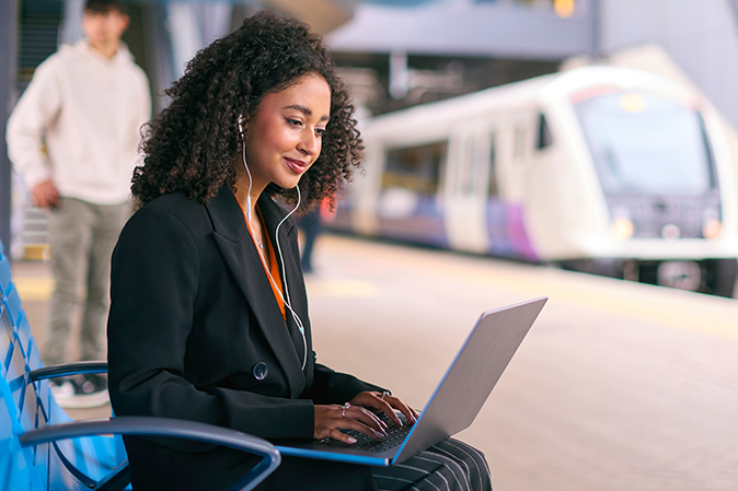 Businesswoman Commuting On Train Platform Working On Laptop Wearing Earphones