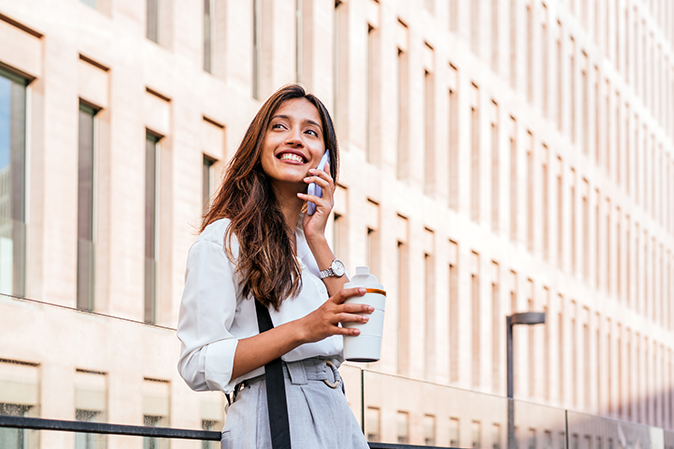 Young woman outside on her phone holding a coffee