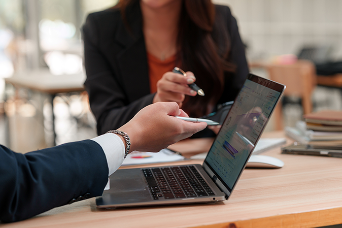 Two business people pointing to a laptop while reviewing a document