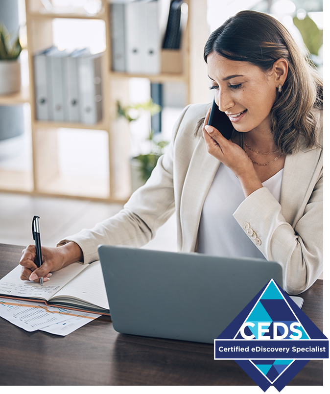Young woman on a cell phone taking notes in front of a laptop