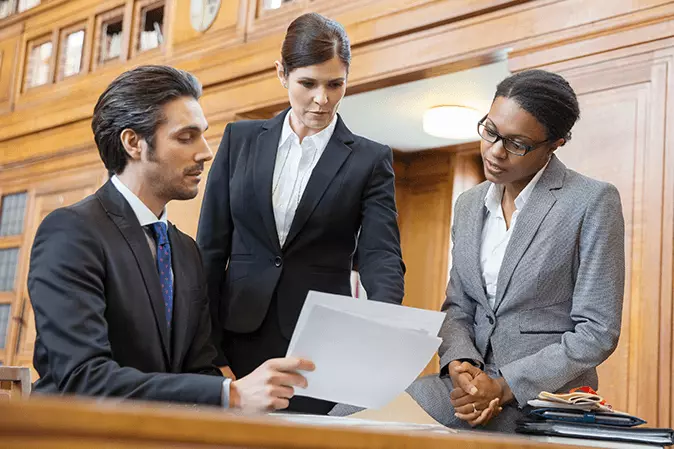 Three lawyers reviewing legal documents together in a courtroom