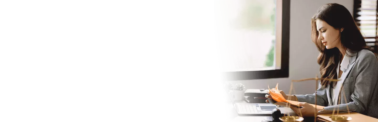 Female lawyer reviewing legal documents at her desk beside a laptop in an office