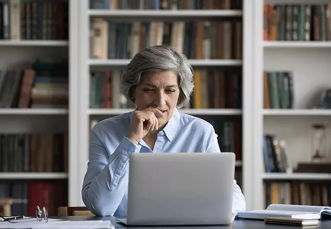 Female law professor reviewing material on a laptop while seated at a desk in front of bookshelves