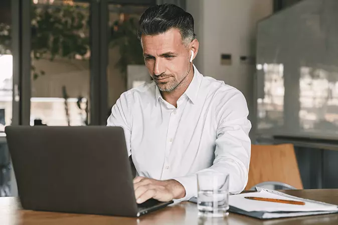 Man wearing earbuds working on a laptop at a desk in an office
