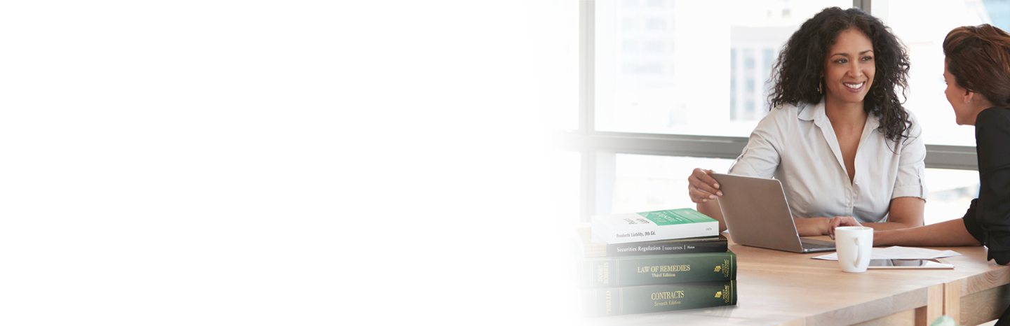 Two women in an office looking at a laptop with a stack of West Academic textbooks on the table