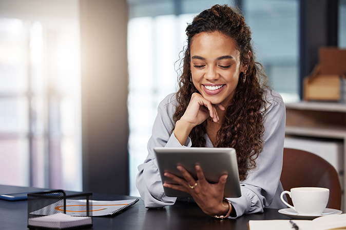 Young woman smiling sitting at a desk holding a tablet