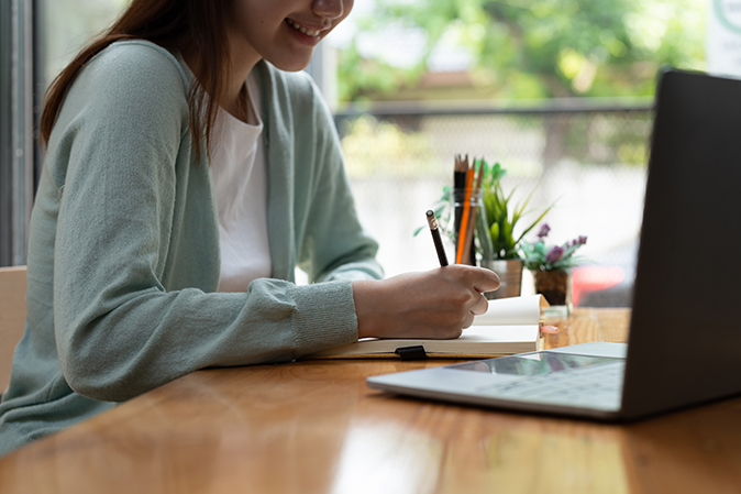Young Asian girl student wears headphones writing on the notebook to study language online watch and listen to the lecturer, webinar via video call e-learning at home.